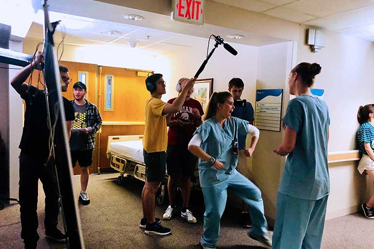 Student filmmakers carry equipment and record video of actors dressed in scrubs.